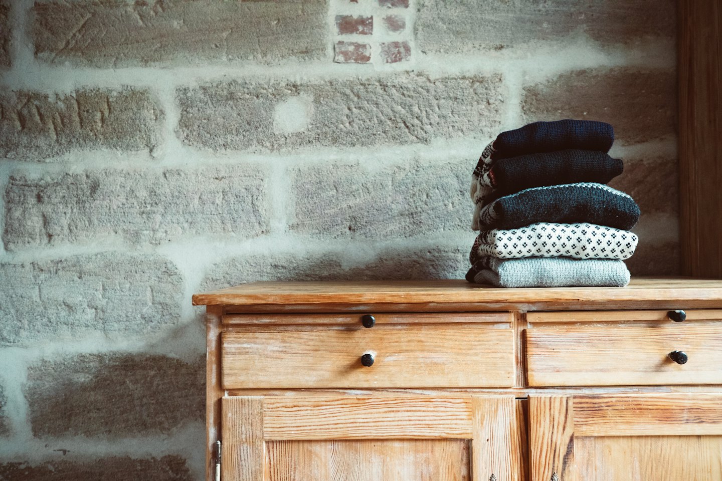 Neatly folded sweaters stacked on a wooden dresser.