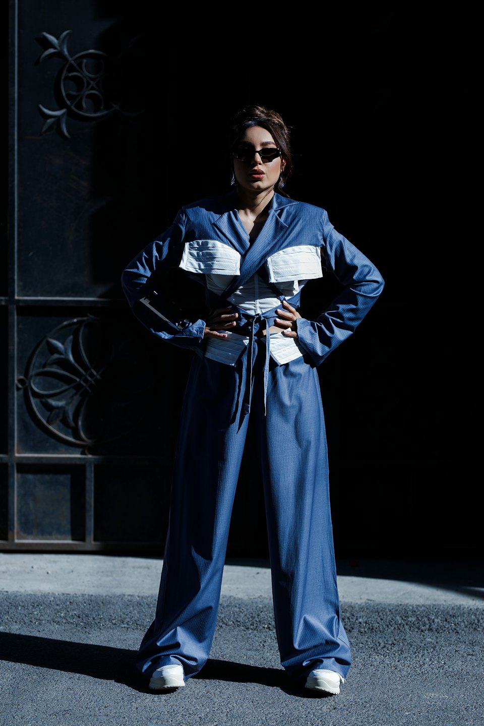 Woman wearing a blue pinstriped pantsuit and sunglasses stands outdoors.