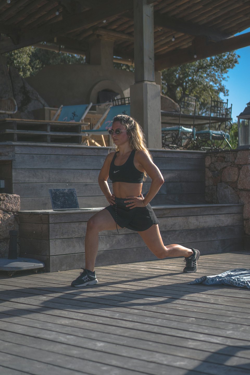 Woman in sportswear lunging on a wooden deck with laptop.