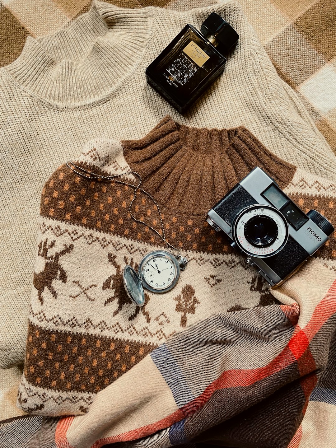 Cozy sweaters, perfume bottle, pocket watch, and camera on a blanket.