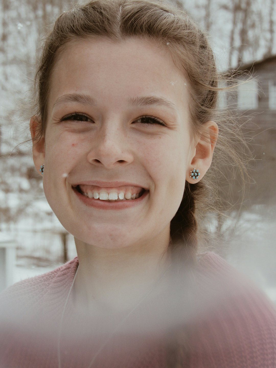 Woman in a pink sweater smiling while light snow falls.