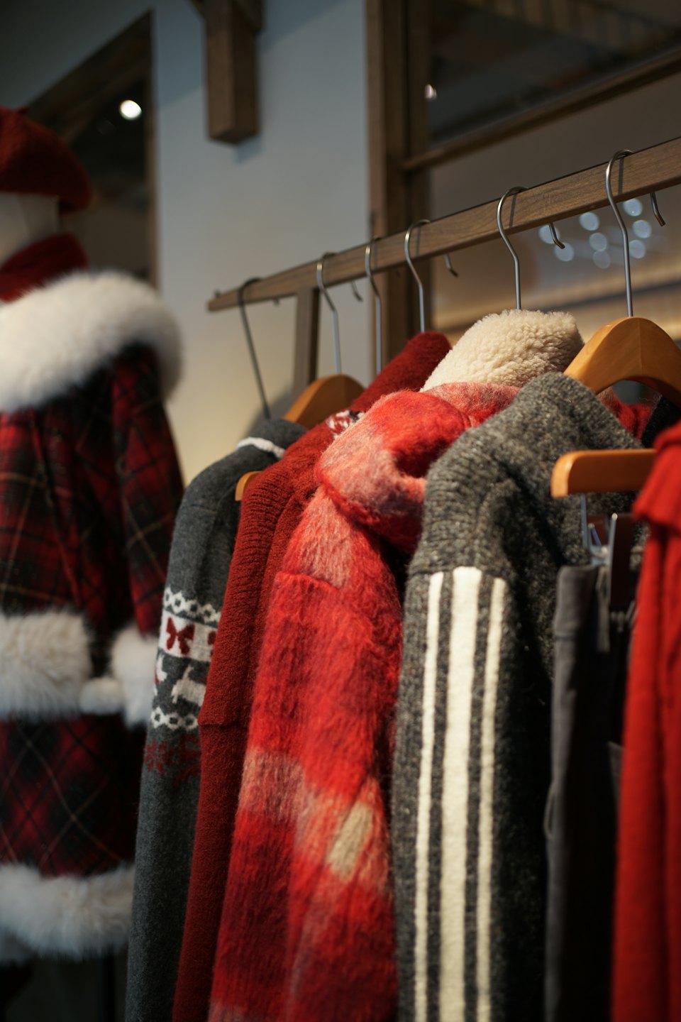 Knitted sweaters and a plaid coat hang on a wooden rack.
