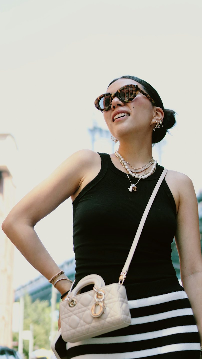 Young woman in striped skirt smiles outdoors with handbag.